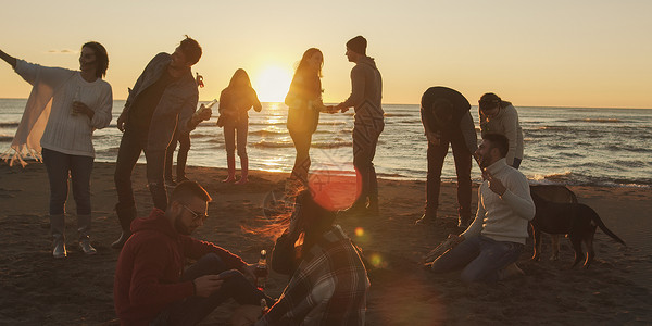 快乐无忧无虑的轻朋友海滩上玩得开心,太阳开始落山的时候篝火旁喝啤酒背景图片