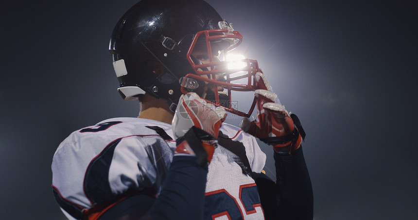美国足球运动员戴上他的保护头盔,以抵御明亮的体育场照明灯图片