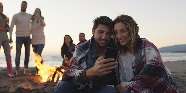 夫妇海滩聚会上用手机朋友喝啤酒,玩得开心图片