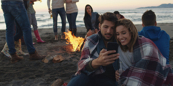 聚是一团火夫妇海滩聚会上用手机朋友喝啤酒,玩得开心背景
