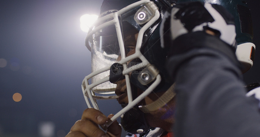 美国足球运动员戴上他的保护头盔,以抵御明亮的体育场照明灯图片
