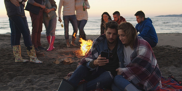 夫妇海滩聚会上用手机朋友喝啤酒,玩得开心高清图片