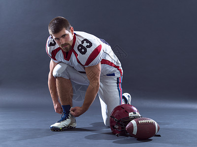 强壮肌肉的美国足球运动员把他的鞋带系灰色上图片