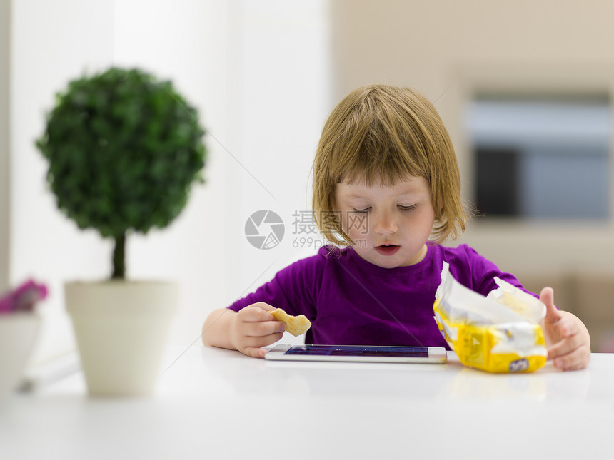 可爱的小女孩家平板电脑上玩游戏时吃饼干图片