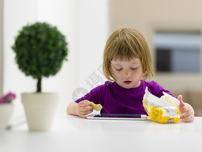 可爱的小女孩家平板电脑上玩游戏时吃饼干图片