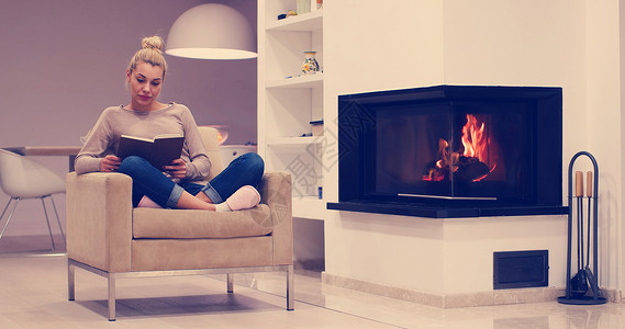个寒冷的秋日,轻美丽的女人坐家里的壁炉前看书图片