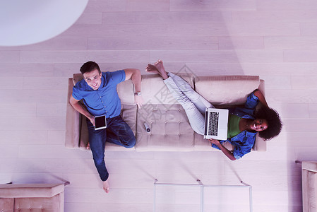轻的多民族夫妇豪华的客厅里放松,用平板电脑笔记本电脑的顶部视图图片