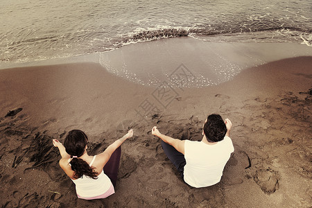 轻的夫妇海滩上清晨以莲花的姿势冥想瑜伽图片