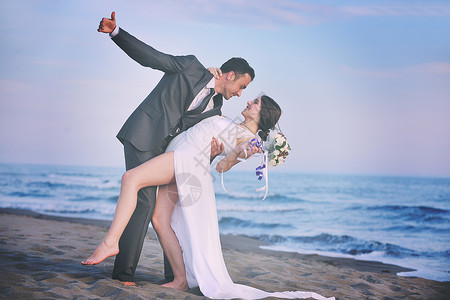 快乐,刚刚结婚的轻夫妇庆祝,并美丽的海滩日落玩得开心背景图片