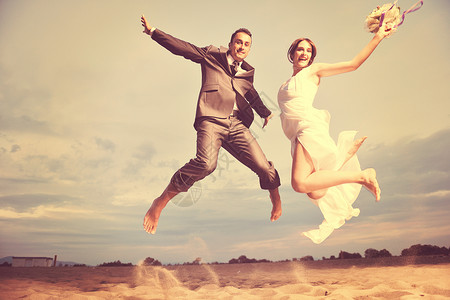 快乐,刚刚结婚的轻夫妇庆祝,并美丽的海滩日落玩得开心图片
