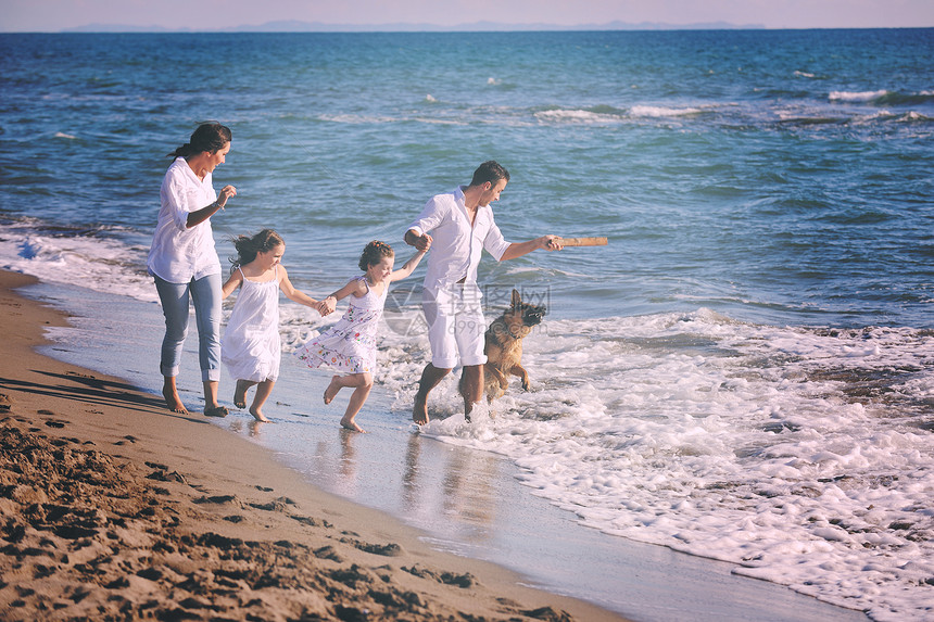 穿着白色衣服的快乐的轻家庭美丽的海滩度假时漂亮的狗玩图片
