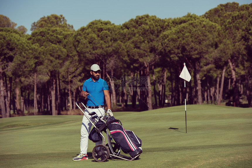 美丽的阳光明媚的天,英俊的中东高尔夫球员带着车轮袋球场上行走高尔夫球手用轮袋行走图片
