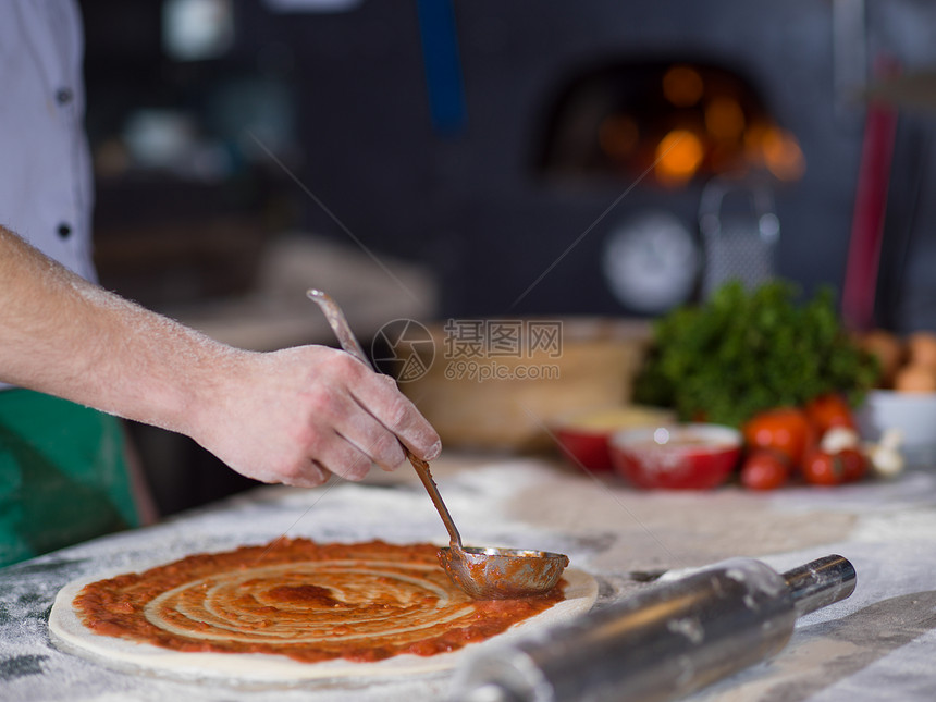 厨师用番茄酱涂抹比萨饼图片