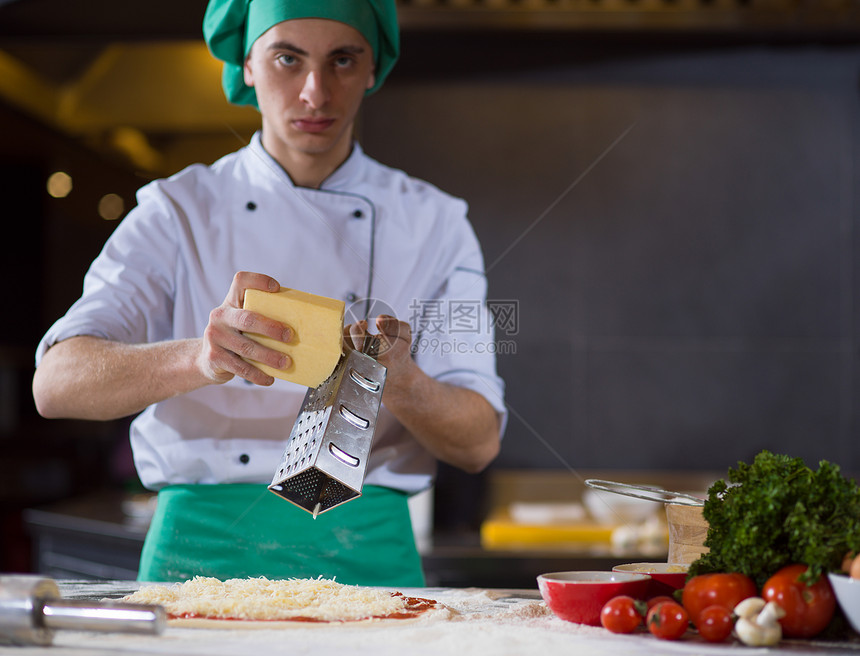厨师把奶酪洒厨房桌子上的新鲜披萨上厨师新鲜披萨上洒奶酪图片