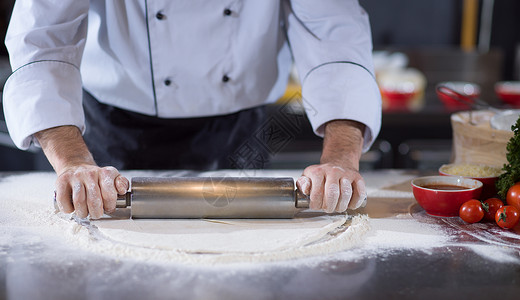 滚压厨师准备,用擀杖洒满粉的桌子上擀饼厨师用擀杖为比萨饼准备背景