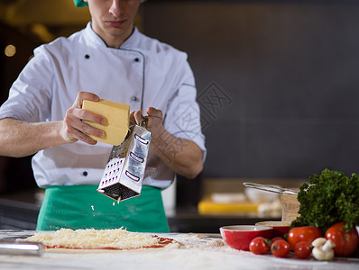 厨师把奶酪洒厨房桌子上的新鲜披萨上厨师新鲜披萨上洒奶酪图片