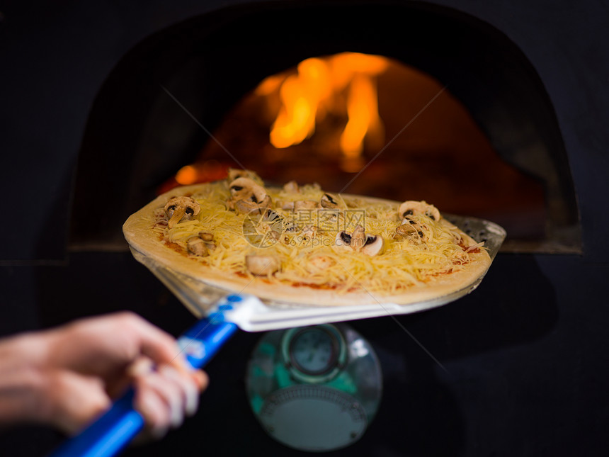 厨师用木柴火焰把美味的比萨饼放砖木烤箱里厨师把美味的比萨饼放砖木烤箱里图片