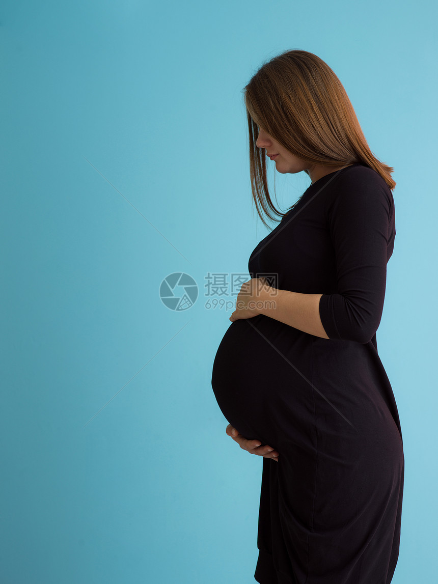 蓝色背景下孕妇的肖像幸福孕妇的肖像,双手放蓝色背景上腹部图片