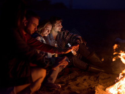 轻的夫妇晚上朋友坐海滩上的篝火旁喝啤酒夫妇晚上海滩上朋友享受图片