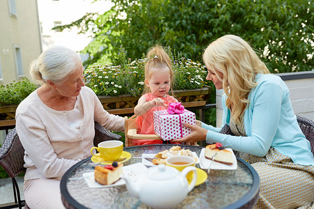 家庭世代人的快乐的祖母母亲咖啡馆餐馆露台给小女儿送礼物快乐的母亲咖啡馆给小女儿送礼物背景图片