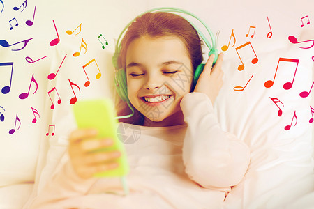 耳机圆球音符人,孩子技术快乐的微笑女孩与智能手机耳机躺床上听音乐的音符戴着耳机床上听音乐的女孩背景