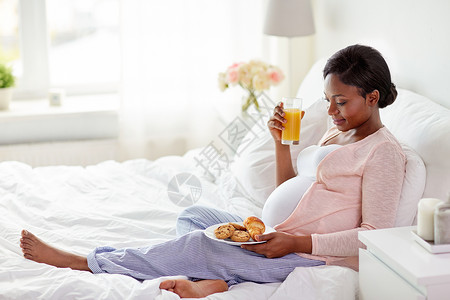 怀孕,人饮食快乐怀孕的非裔美国妇女喝橙汁与糕点床上家孕妇床上喝橙汁糕点图片