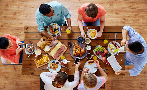 早餐,技术家庭群智能手机的人桌子上吃拍照食物智能手机的人桌子上吃食物图片