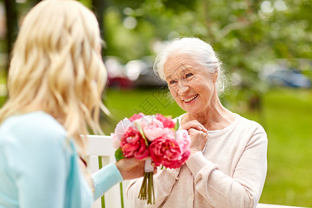 家庭,假期人的快乐的微笑的轻女儿送花给她的老母亲坐公园的长凳上女儿公园给迈的母亲送花背景图片