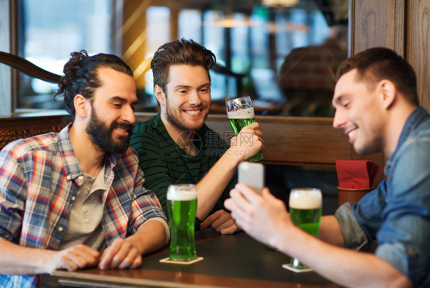 休闲,帕特里克日技术快乐的男朋友与智能手机喝绿色啤酒酒吧酒吧智能手机的朋友酒吧喝绿色啤酒图片