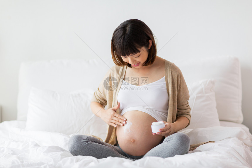 怀孕,人产妇的快乐的怀孕亚洲妇女应用拉伸标记奶油腹部快乐的亚洲孕妇肚子上涂奶油图片