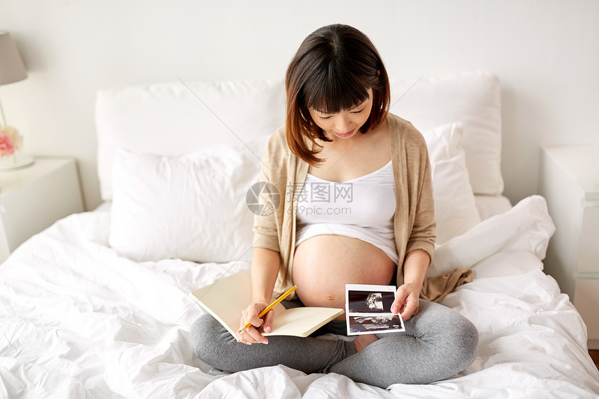怀孕人们的快乐的亚洲孕妇与胎儿超声图像笔记本日记床上家孕妇家里胎儿超声图像图片