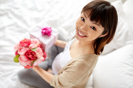 怀孕,假期人的快乐的怀孕亚洲妇女与礼品盒鲜花床上家里快乐的亚洲孕妇带着礼物鲜花背景图片