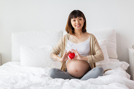 怀孕,爱,人期望的快乐的怀孕亚洲妇女坐床上,红心家快乐的亚洲孕妇,红心床上图片