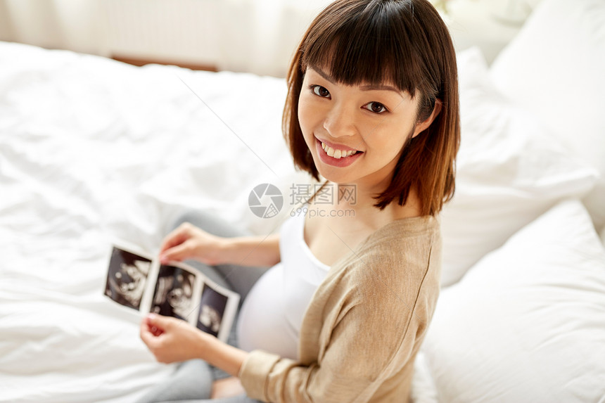 怀孕人们的快乐怀孕的亚洲妇女与胎儿超声图像床上家里孕妇家里胎儿超声图像图片