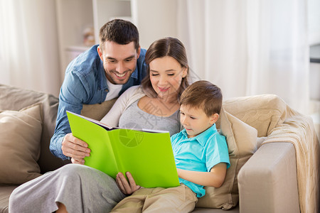 沙发上的书人们家庭的快乐的母亲,父亲小儿子家沙发上看书家快乐的家庭读物背景