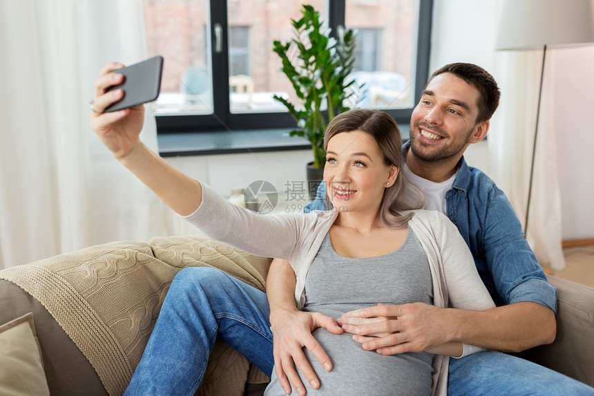 技术人的快乐的男人他怀孕的妻子家里用智能手机自拍男人孕妇家自拍图片