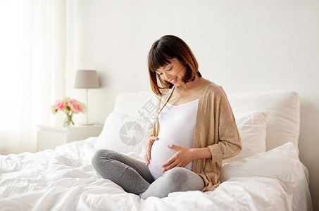 怀孕,人母的快乐的亚洲孕妇坐家里的卧室床上快乐的亚洲孕妇坐家里的床上图片