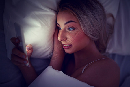 晚上轻的女人家里卧室的床上智能手机图片