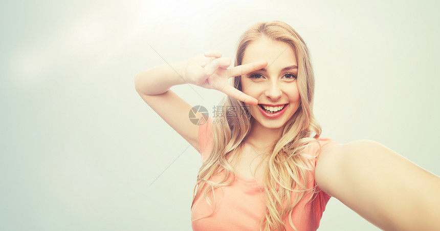 情感,表情人的快乐的微笑轻女子自拍平手标志灰色背景微笑的女人自拍并展示平标志图片