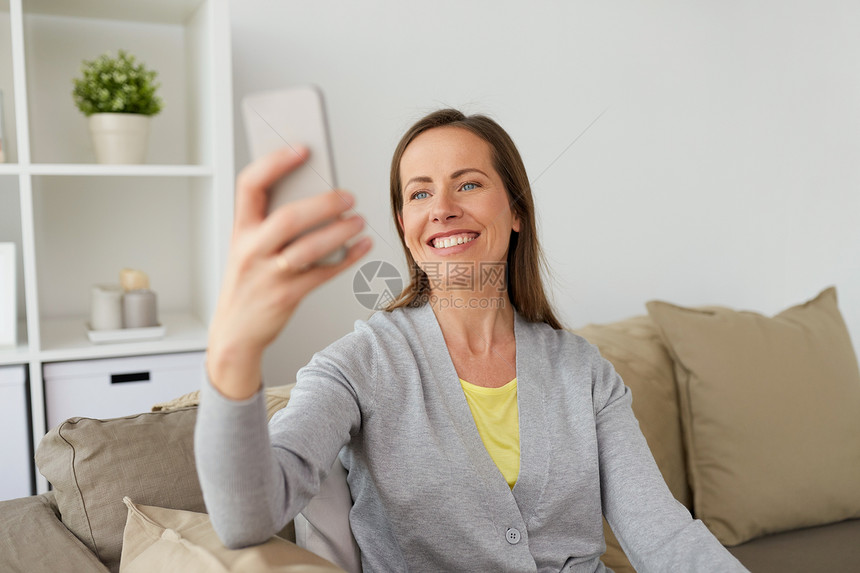 人,技术沟通快乐的中妇女家里用智能手机自拍快乐的女人家里用智能手机自拍图片