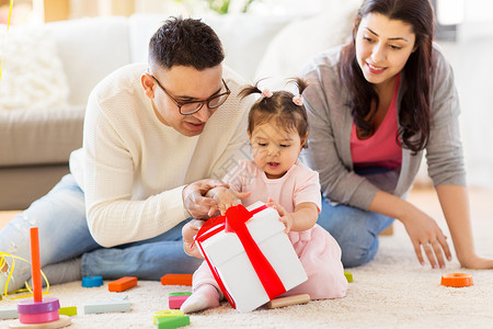 家庭,假期人的母亲,父亲快乐的小女儿家里的生日聚会上礼品盒带生日礼物的女婴父母家带生日礼物的女婴父母背景图片