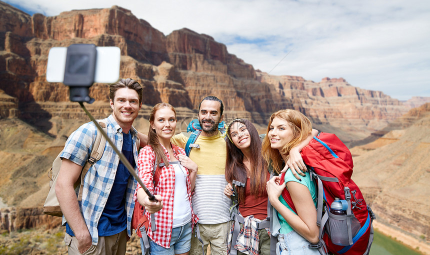 旅行,旅游技术群微笑的朋友,用智能手机大峡谷公园背景的岩石上自拍杆上用背包拍照快乐的旅行者大峡谷自拍快图片