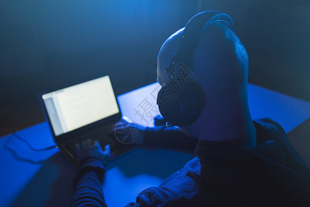 违背网络犯罪,黑客技术黑客与耳机用笔记本电脑进行网络攻击窃听黑暗的房间黑客黑暗的房间里用耳机笔记本电脑上打背景