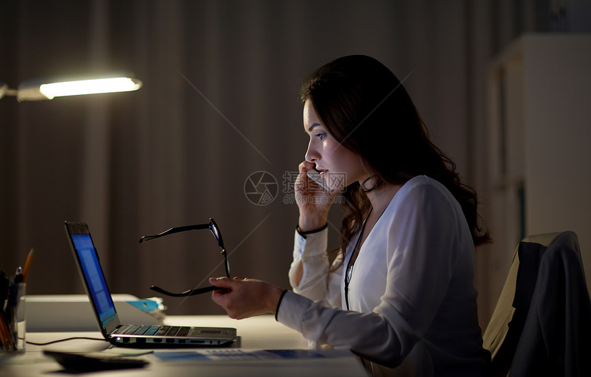 商业,技术,过度工作,截止日期人的女人带着笔记本电脑夜间办公室打电话给智能手机笔记本电脑的女人办公室打电话给智图片