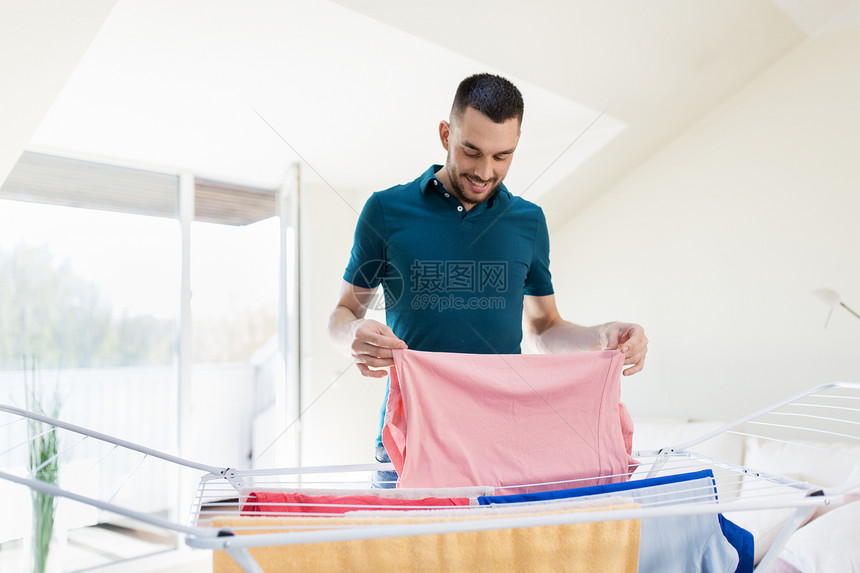 洗衣家庭快乐的人晾衣架上衣服,把它们放家里的篮子里微笑的男人,家里洗衣烘干架微笑的男人,家里洗衣烘图片