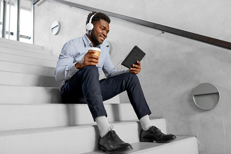 音乐楼梯商业,人技术非裔美国商人戴着耳机平板电脑,电脑办公室咖啡休息时听音乐戴耳机平板电脑的商人戴耳机平板电脑的背景