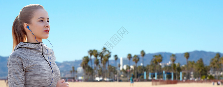 加利福尼亚威尼斯海滩背景上女人戴着耳机听音乐跑步背景图片