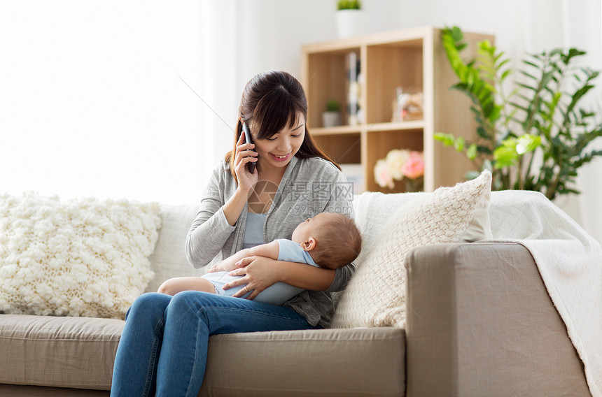 家庭,技术母亲的快乐的微笑的轻亚洲母亲与熟睡的婴儿打电话家里的智能手机母亲带着婴儿家里打电话给智能手机母亲图片