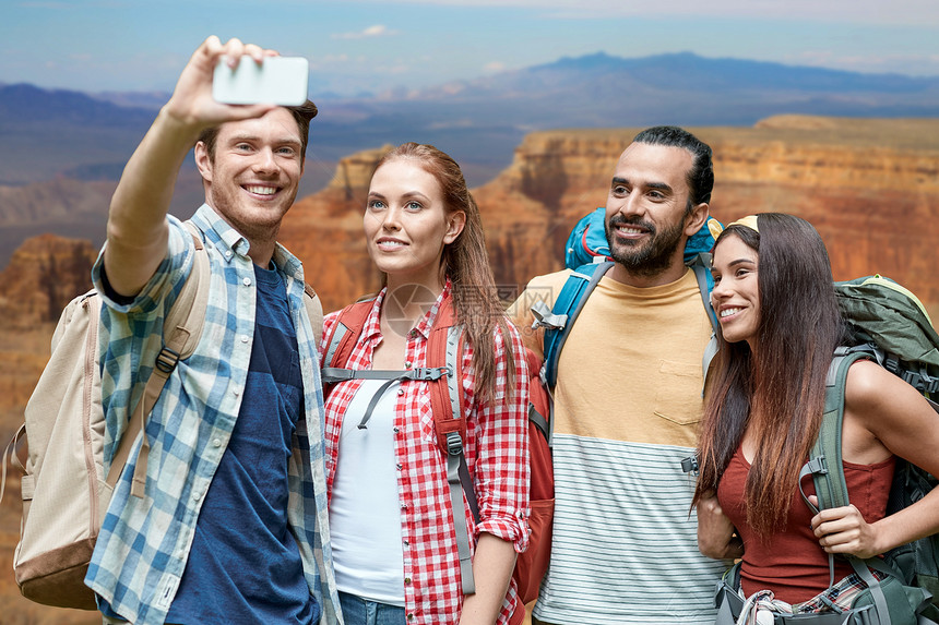 技术,旅游,徒步旅行人的群微笑的朋友,背包大峡谷公园背景下用智能手机自拍背包的朋友用智能手机自拍图片