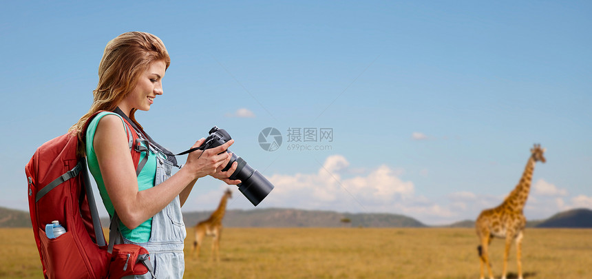 旅行,旅游摄影快乐的轻妇女背包相机拍摄长颈鹿非洲草原背景女人带着背包相机萨凡纳上空图片